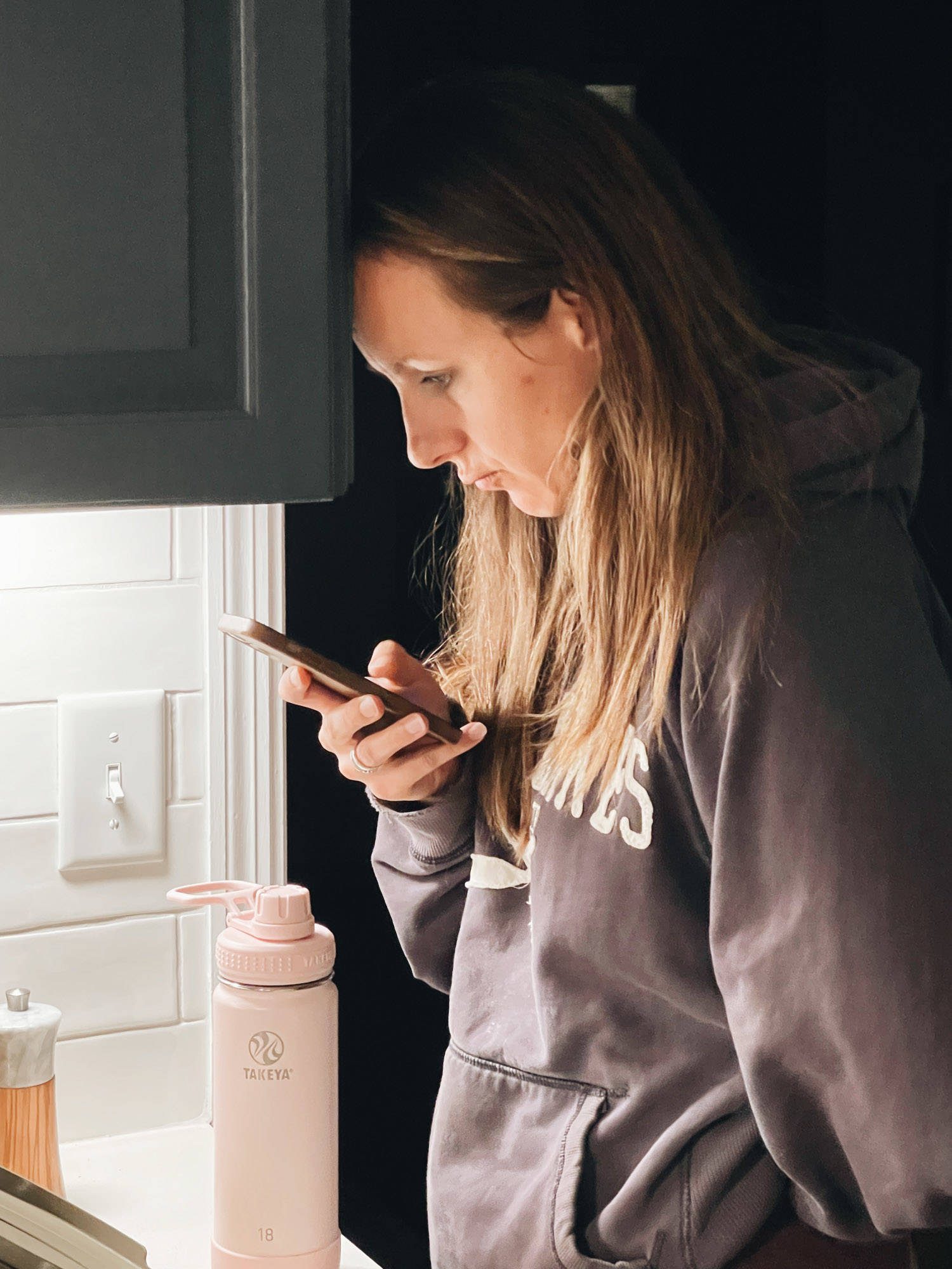 Woman with head against kitchen cabinet looking at phone.